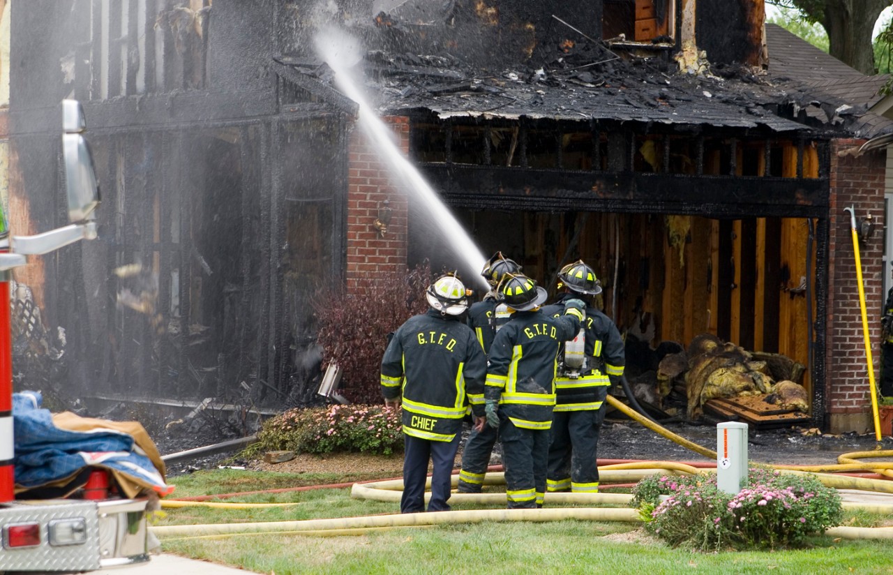 Fire crew extinguishing burned house with water hose.