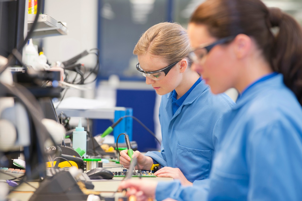 Technicians soldering circuit boards on production line in manufacturing plant